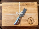 A small board with a monogrammed letter engraved into the bottom right corner, and a small cheese knife attached with twine